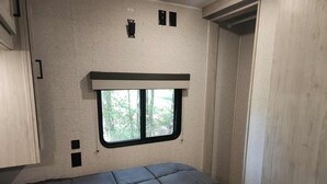 Een compact interieur van een camper, met een bed, een raam en een deur.