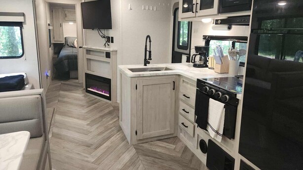 Een ruimtelijk RV-keukentje met een kookplaat, spoelbak en een flatscreen-tv boven het aanrecht.