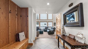 A hallway with a wooden bench, a reception desk, and a view of a living area with a fireplace and a Christmas tree. - Northwest Passage Retreat Ski-In/Ski-Out + Hot Tub (Sandpoint)