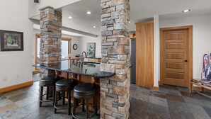 A spacious kitchen with a central island, stone pillars, and a wooden door. - Northwest Passage Retreat Ski-In/Ski-Out + Hot Tub (Sandpoint)