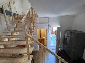 Een houten trap die leidt naar een badkamer, met een wastafel en toilet zichtbaar door een geopende deur.