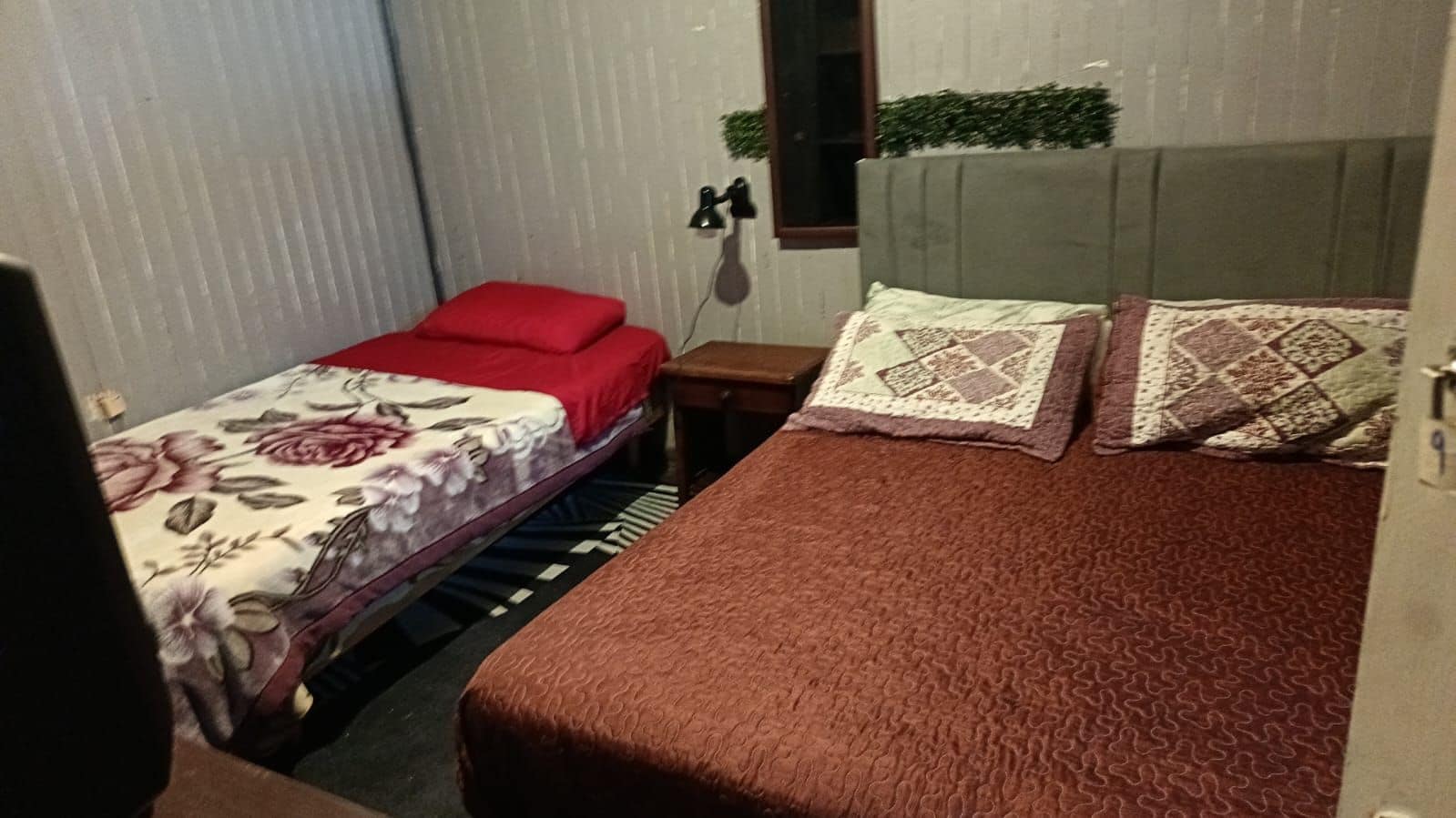 A bedroom with two beds, one with a floral bedspread and red pillows, the other with a brown bedspread and patterned pillows.