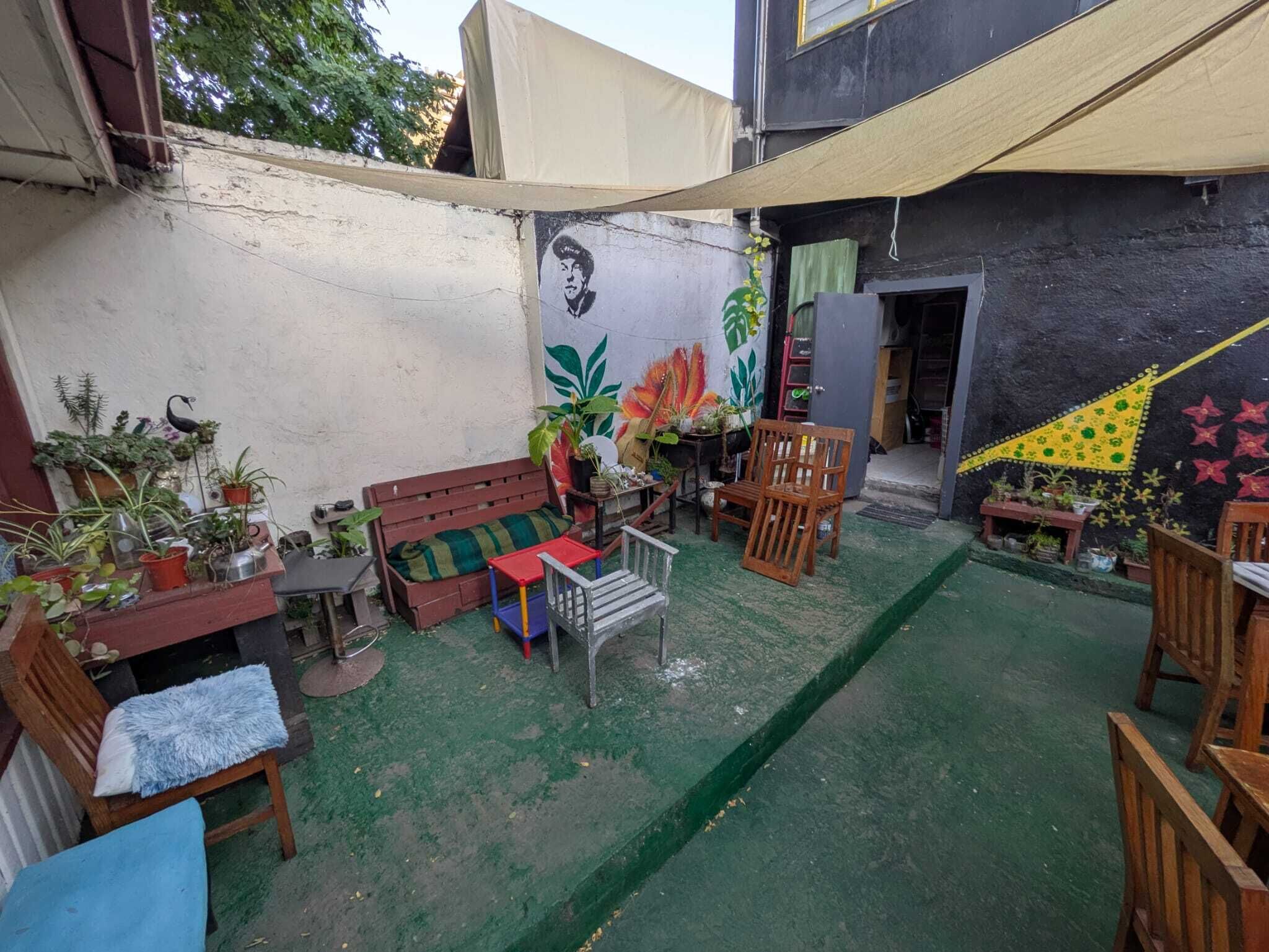 Un patio con césped artificial verde, un banco de madera, una mesita y varias plantas en macetas.