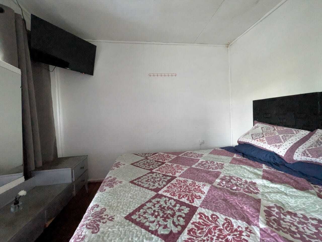 A bedroom with a bed, a dresser, a mirror, and a wall-mounted TV.