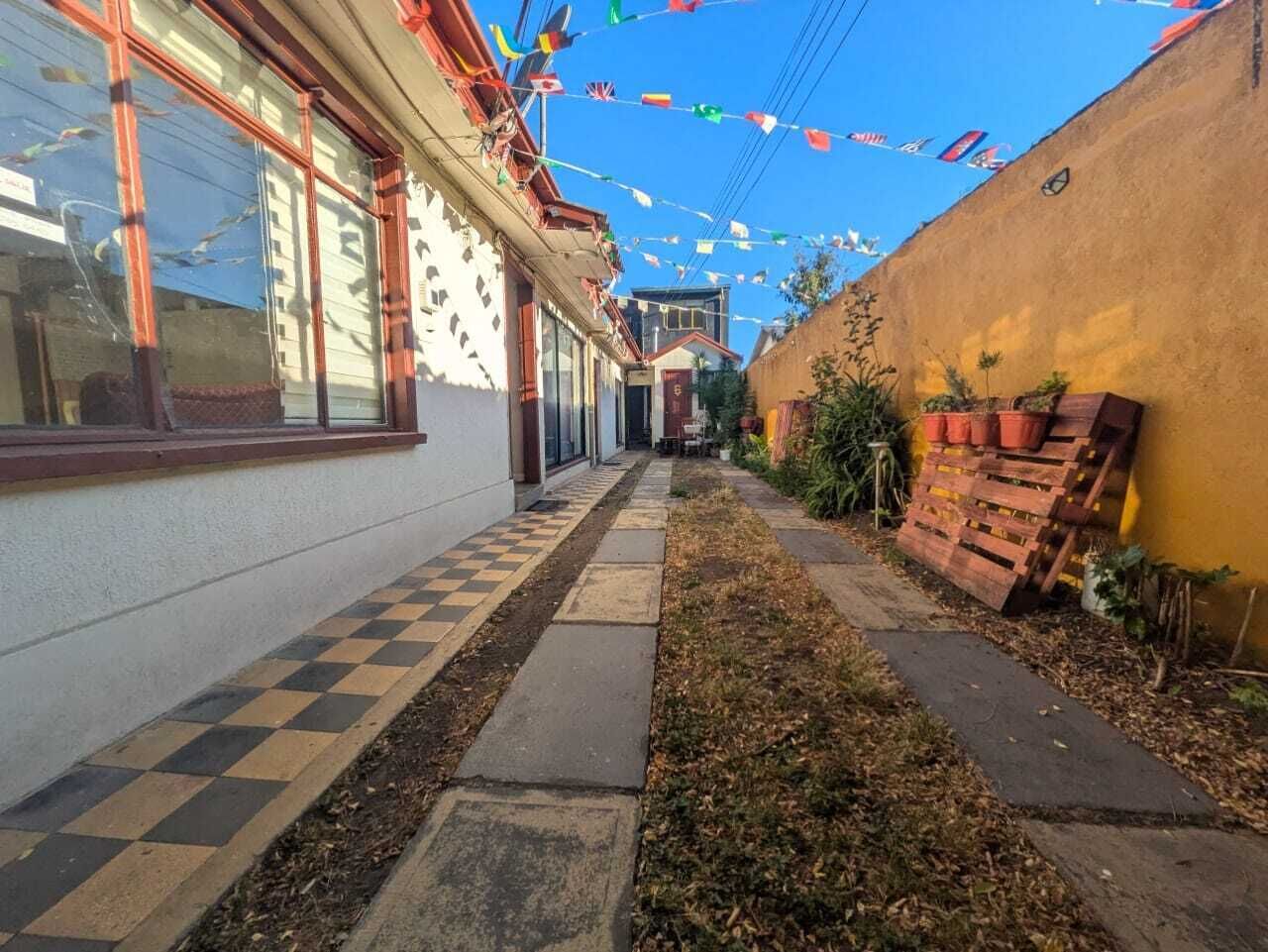 Uma passagem estreita com um caminho quadriculado, ladeada por edifícios com grandes janelas e uma parede amarela de um lado.