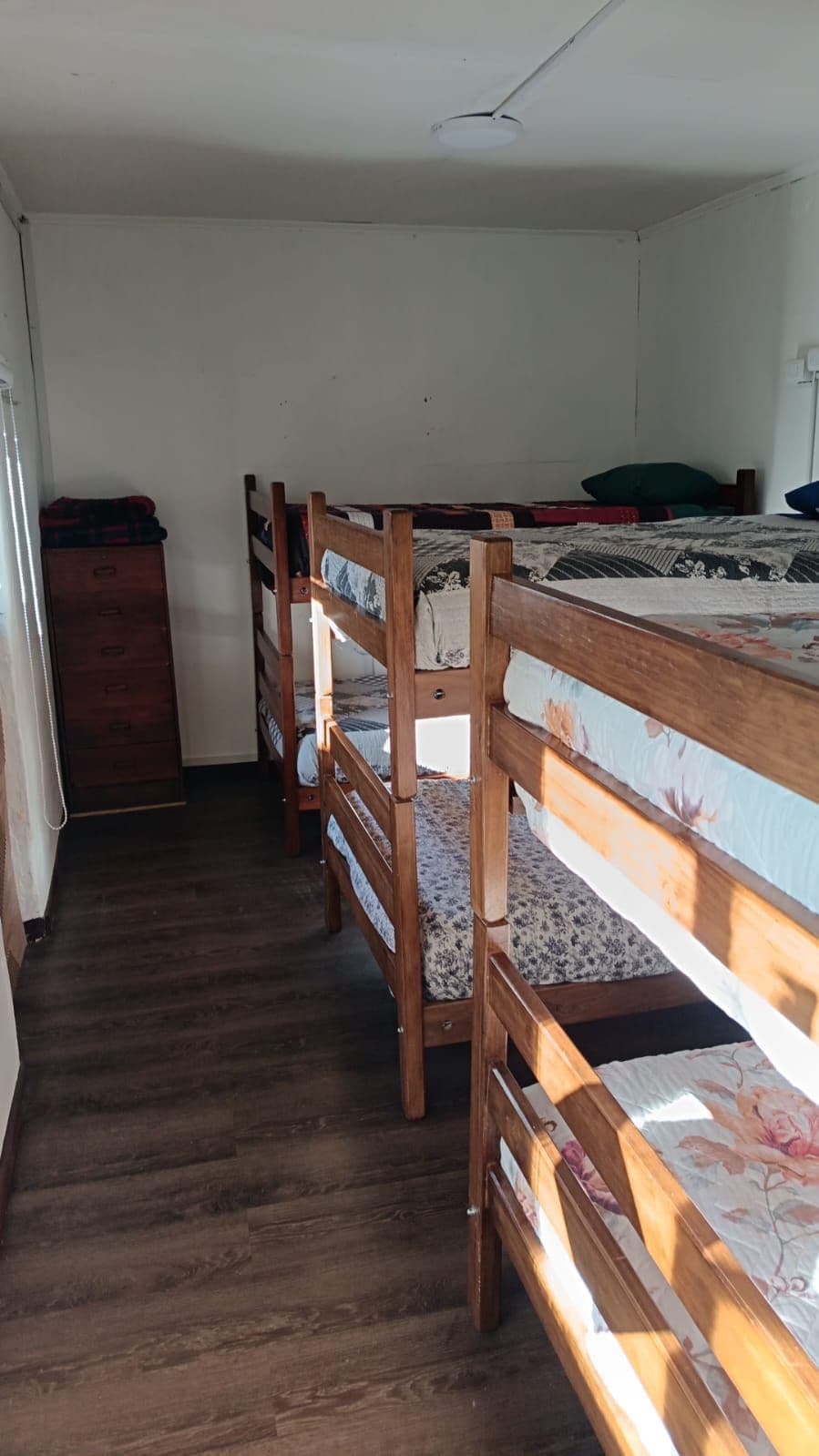 Une chambre de dortoir avec des lits superposés, une commode en bois et une fenêtre.