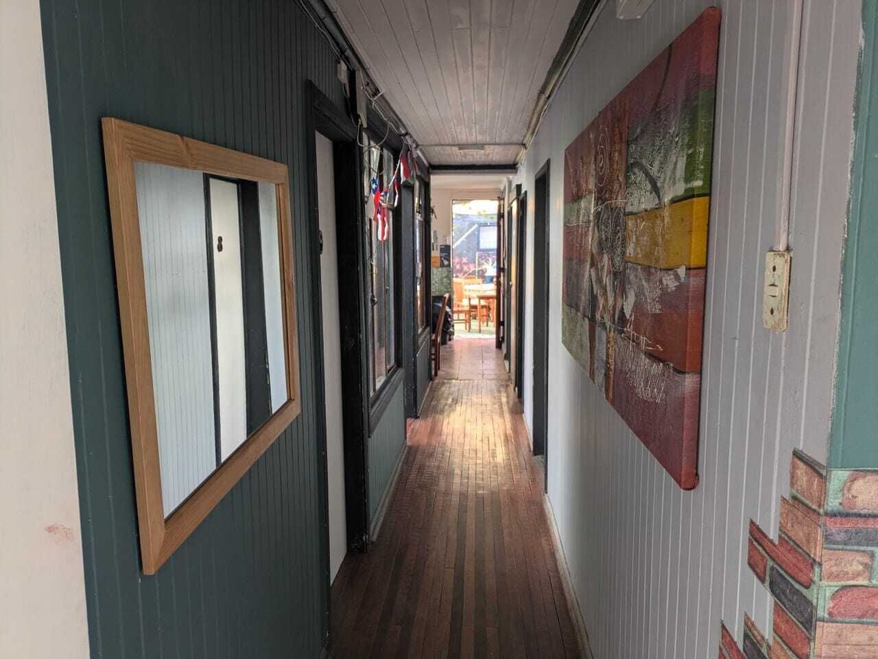 A hallway with wooden flooring, a door with a wooden frame, and a wall with a colorful abstract painting.