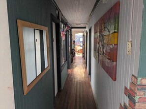 Un pasillo con suelo de madera, una puerta con marco de madera y una pared con un cuadro abstracto de colores.