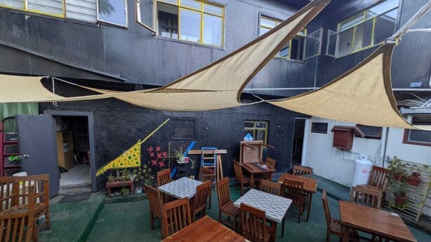 Un área de estar al aire libre con mesas y sillas, protegida por grandes toldos, y una escalera que conduce a un nivel superior.