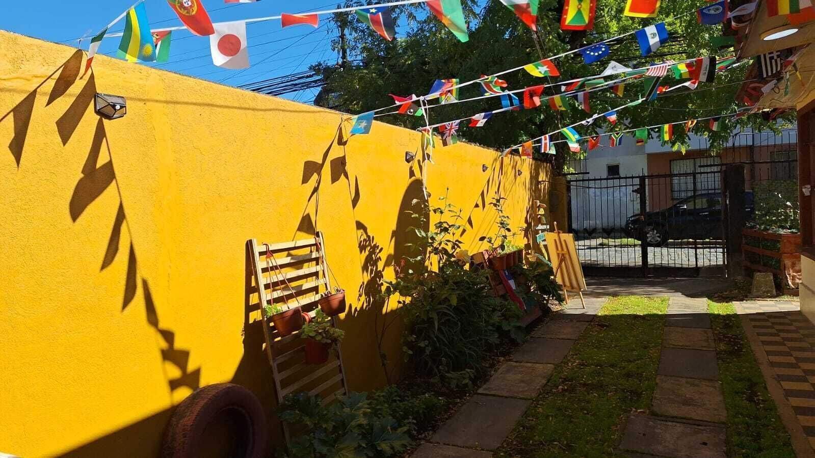 A yellow wall with a wooden ladder and potted plants. Flags are strung above.