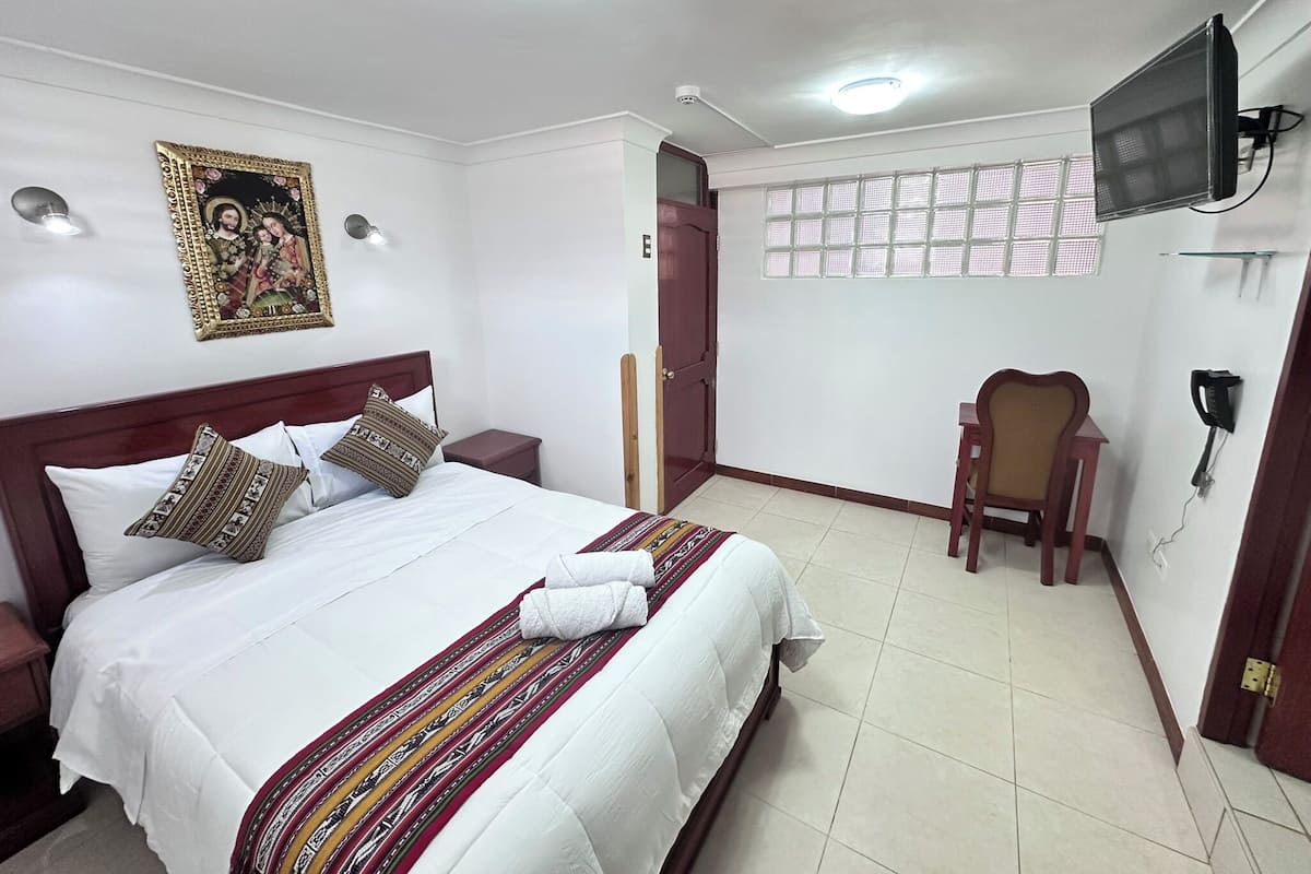 A hotel room with a bed, a chair, a television, and a window with a view.