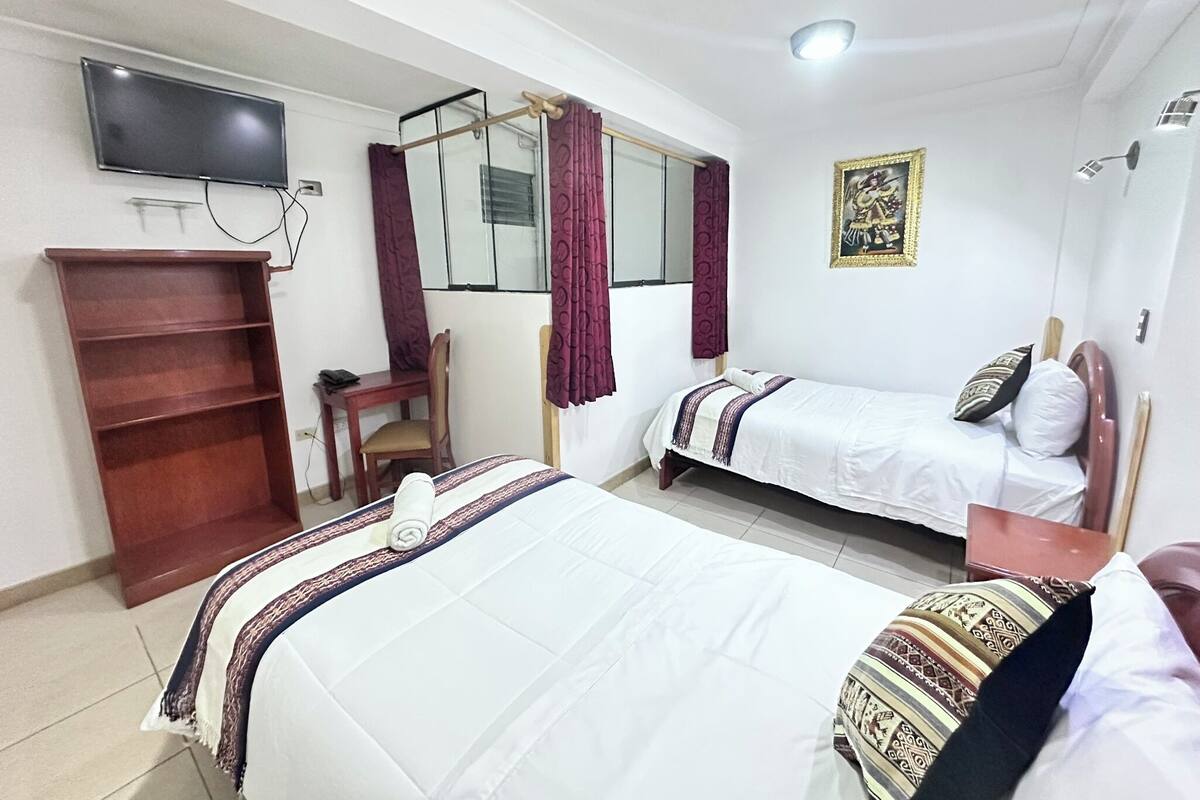 A hotel room with two beds, a TV, a desk, and a chair.