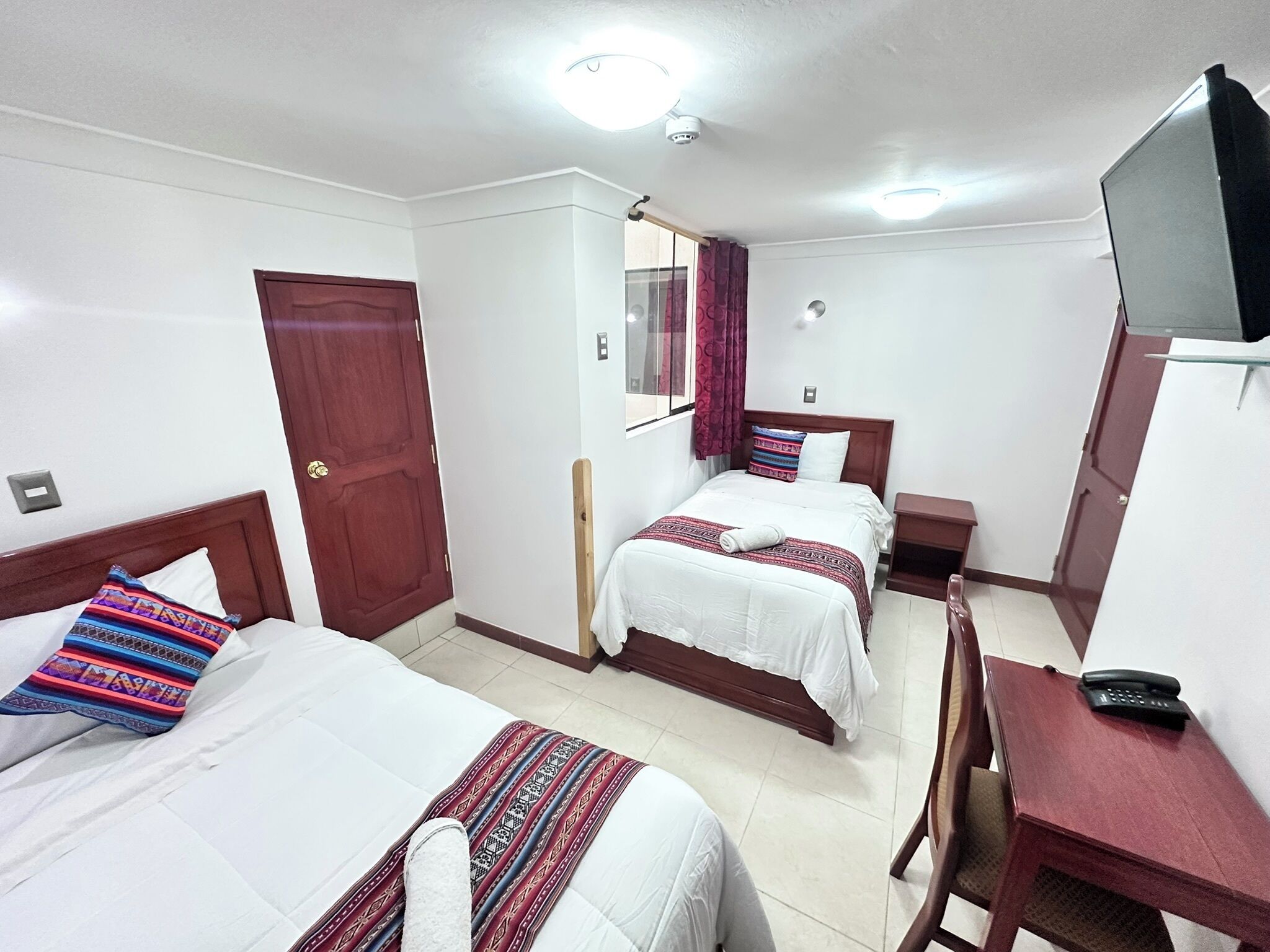 Habitación de hotel con dos camas, un escritorio, una silla, un televisor y una puerta.