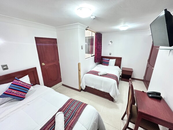 A hotel room with two beds, a desk, a chair, a TV, and a door.