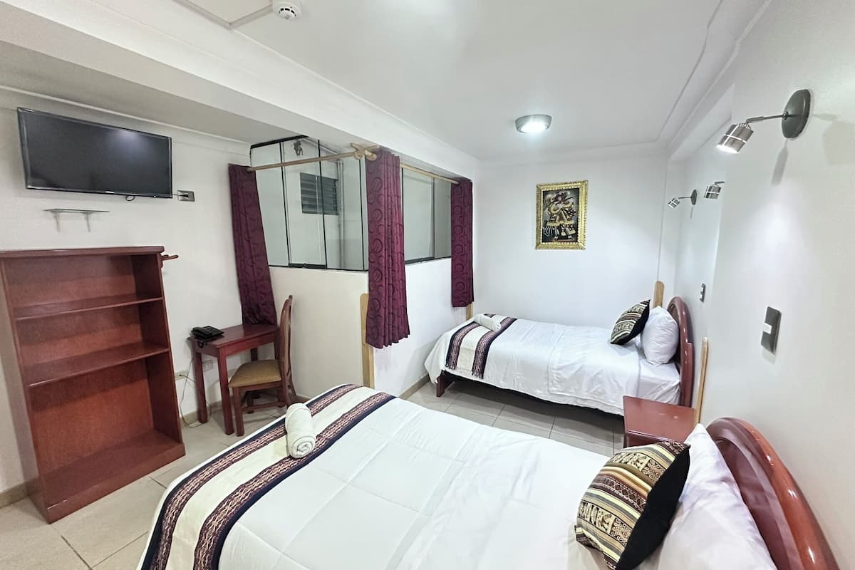 A hotel room with two beds, a TV, a desk, and a chair.