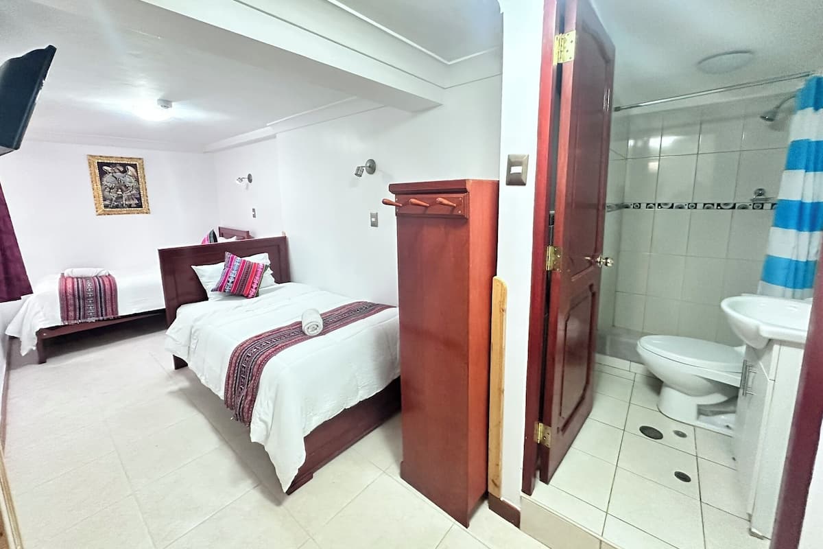A hotel room with two beds, a bathroom with a shower, and a toilet.