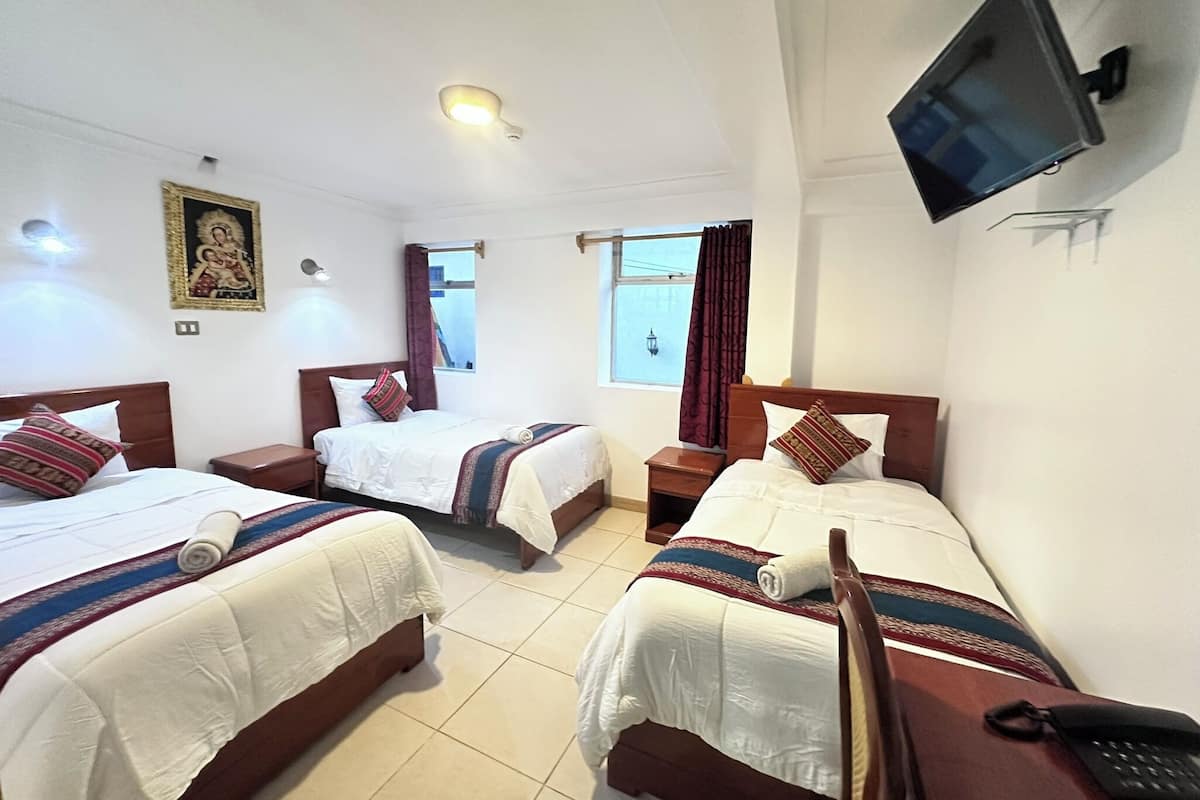 A hotel room with two beds, a television mounted on the wall, and a window with curtains.