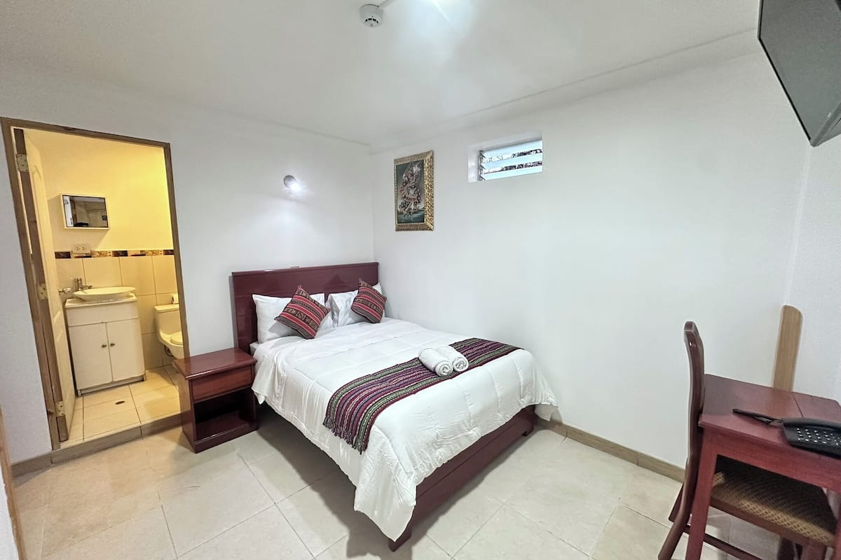 A hotel room with a bed, a desk, a chair, a small bathroom, and a ceiling light.
