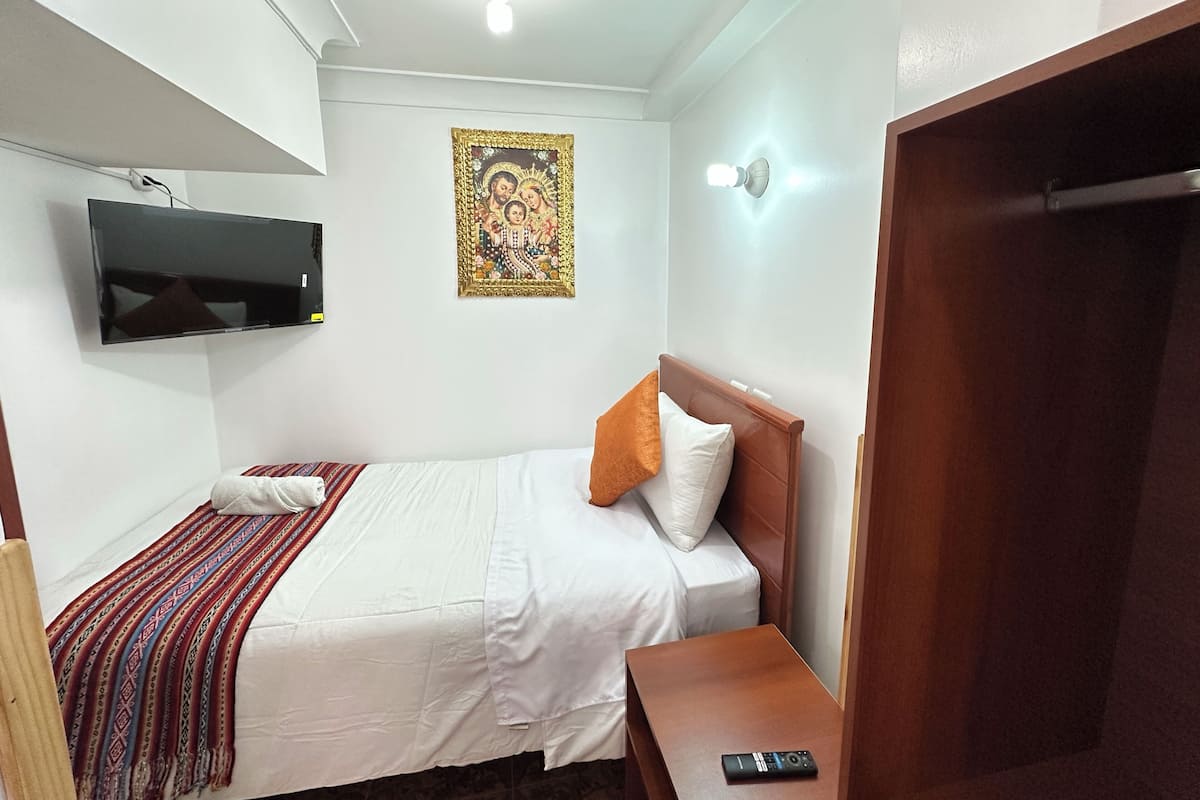 A hotel room with a bed, a bedside table, a TV mounted on the wall, and a ceiling light.