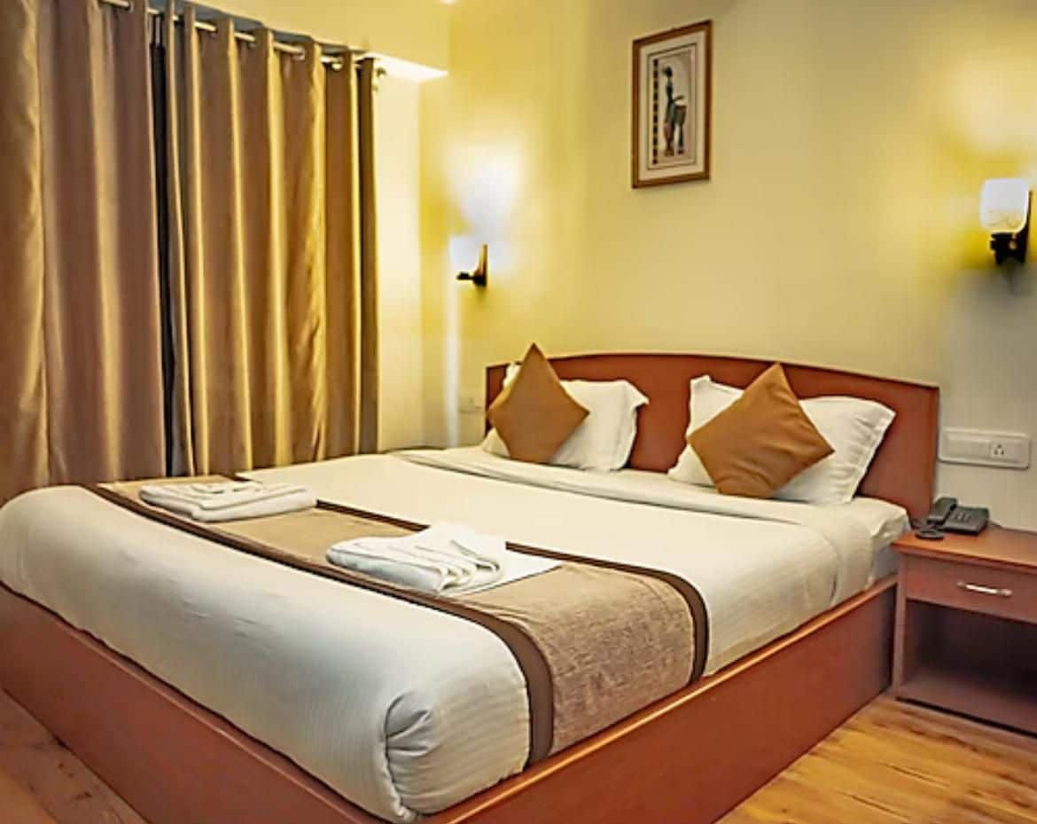 Una habitación de hotel con cama, mesita de noche, lámpara y cortina.