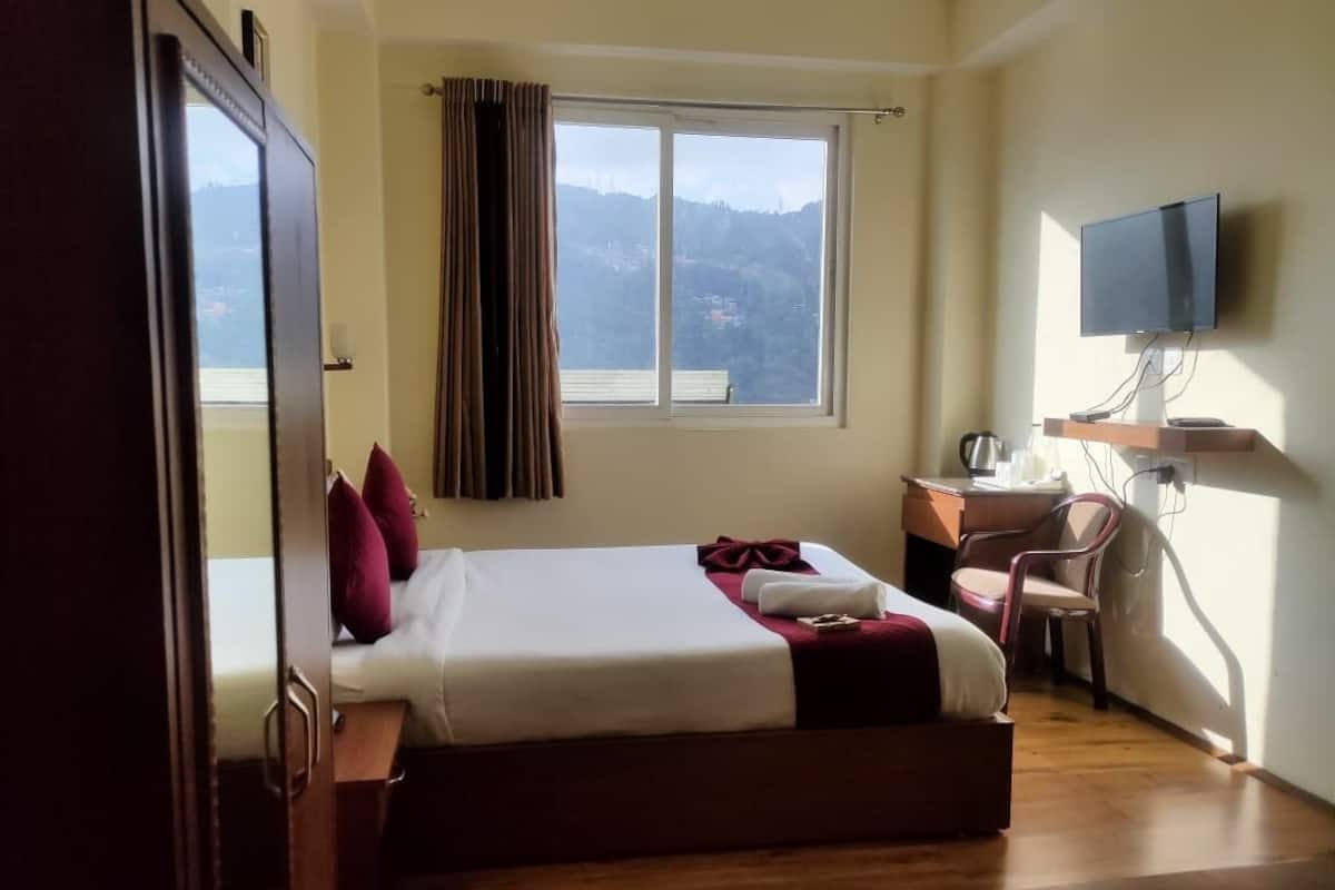 A hotel room with a bed, a desk, a chair, a television, and a window with a mountain view.