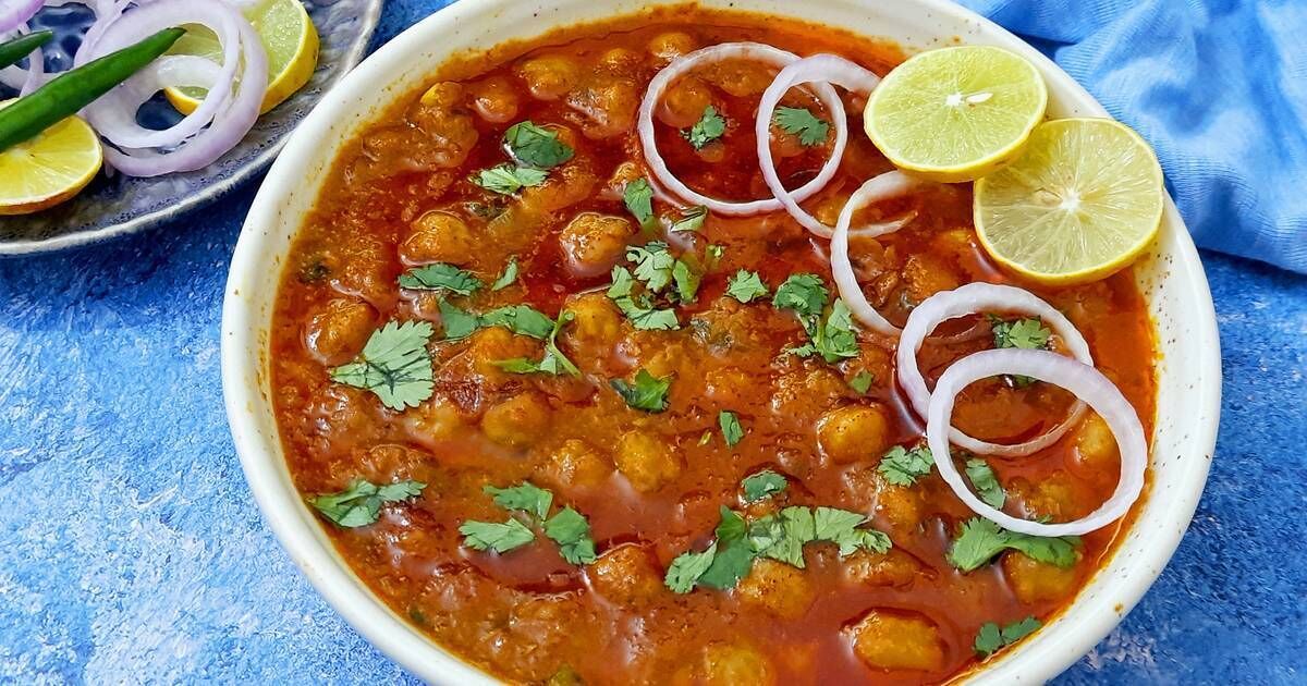 A bowl of chickpea curry garnished with onions and cilantro, served with a side of sliced onions and a lime wedge.