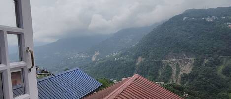 A view from a window overlooking a mountainous landscape with a red-roofed building and a blue-roofed structure in the distance.