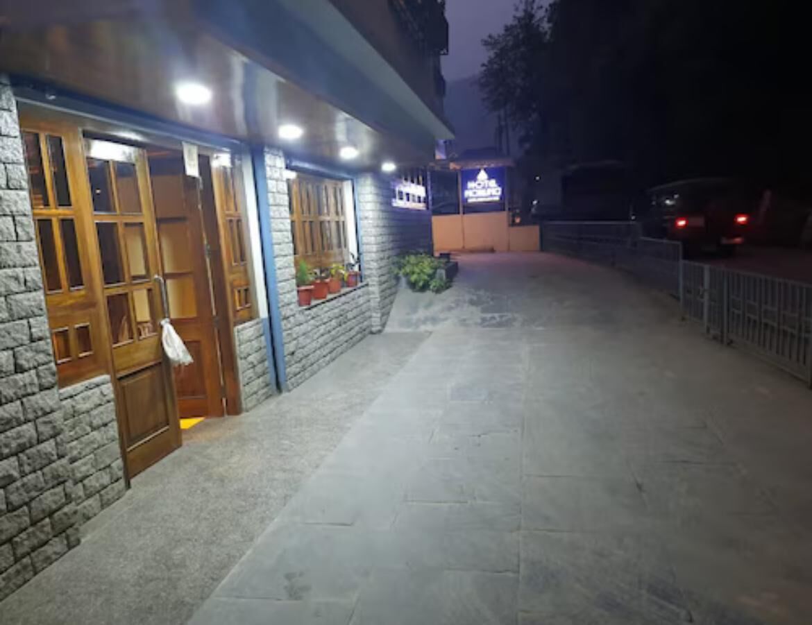 A hotel entrance with a stone facade, wooden doors, and potted plants.