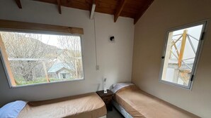 A small, single-room accommodation with two single beds, a window, and a visible power outlet.