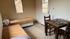 A room with two single beds, a wooden table with chairs, and a window with a view.