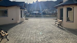 A paved courtyard with benches, buildings with metal roofs, and mountains in the background.
