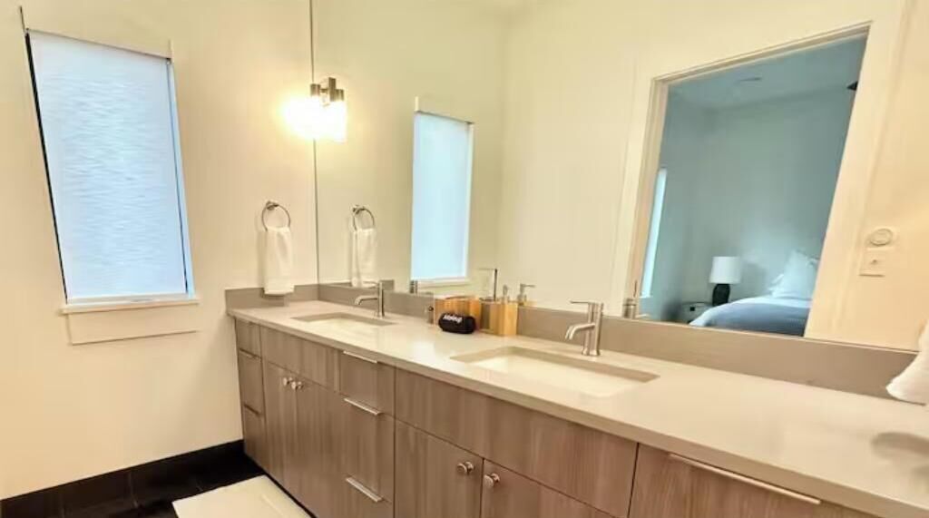 Un bagno moderno con un mobile doppio lavabo, un ampio specchio e una porta che dà accesso a una camera da letto.