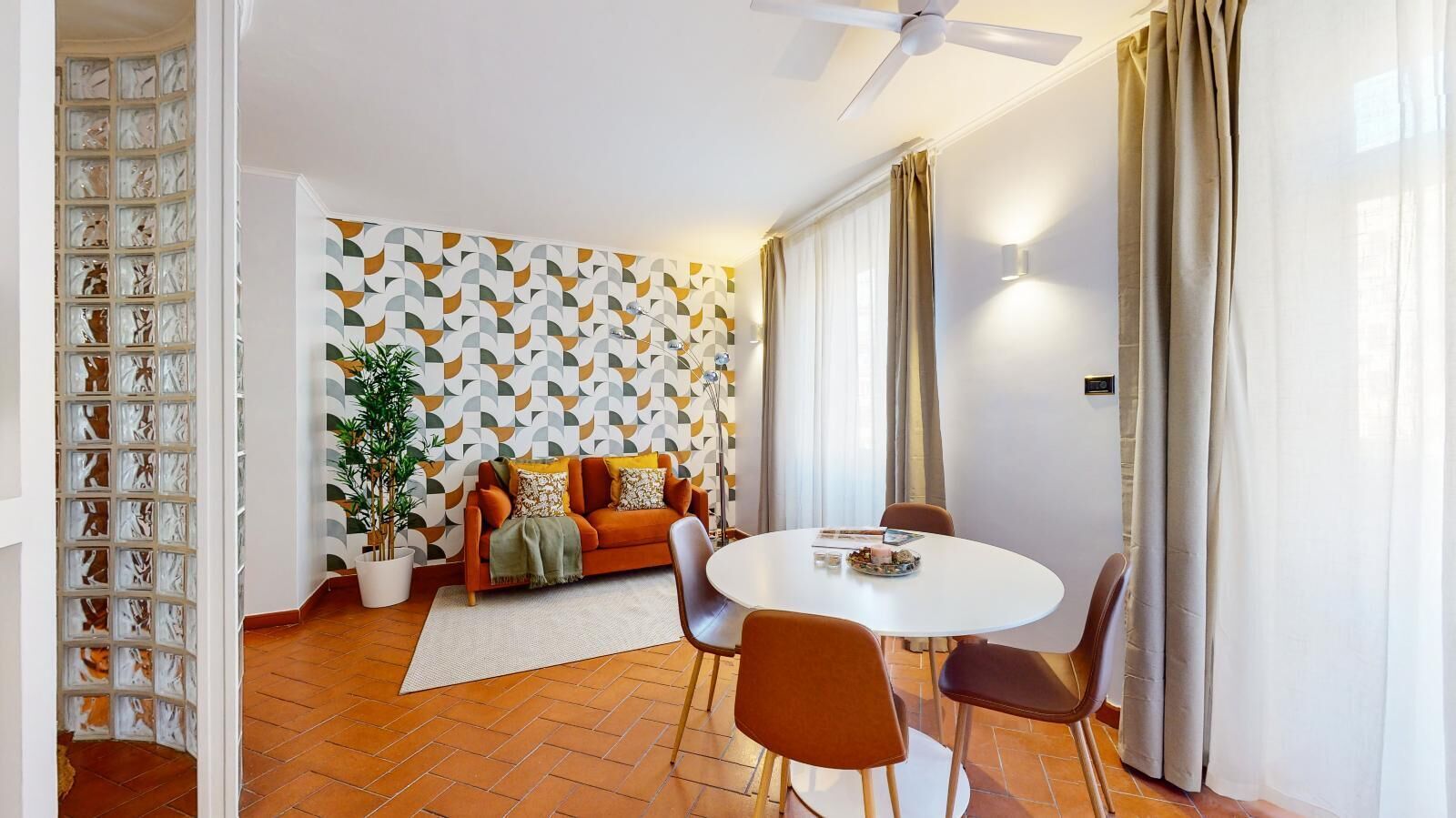A modern living room with a patterned wall, a sofa, a dining table with chairs, and a ceiling fan.