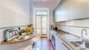 Eine moderne Küche mit weiß gefliesten Wänden, einer Arbeitsplatte aus Granit, Edelstahlgeräten und Blick ins Freie durch eine Glastür.