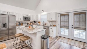 A modern kitchen with white cabinets, stainless steel appliances, and a central island with stools. - Holiday Hills Getaway! (Counce)
