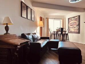 A cozy living room with a leather sofa, a wooden coffee table, and a dining area with chairs and a table.