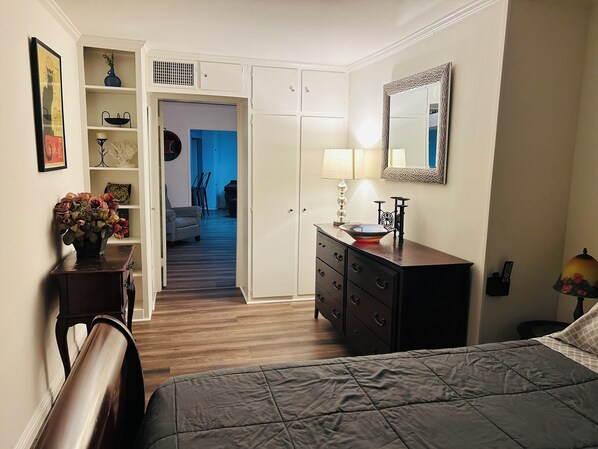 A bedroom with a bed, dresser, vanity, and a hallway leading to another room.