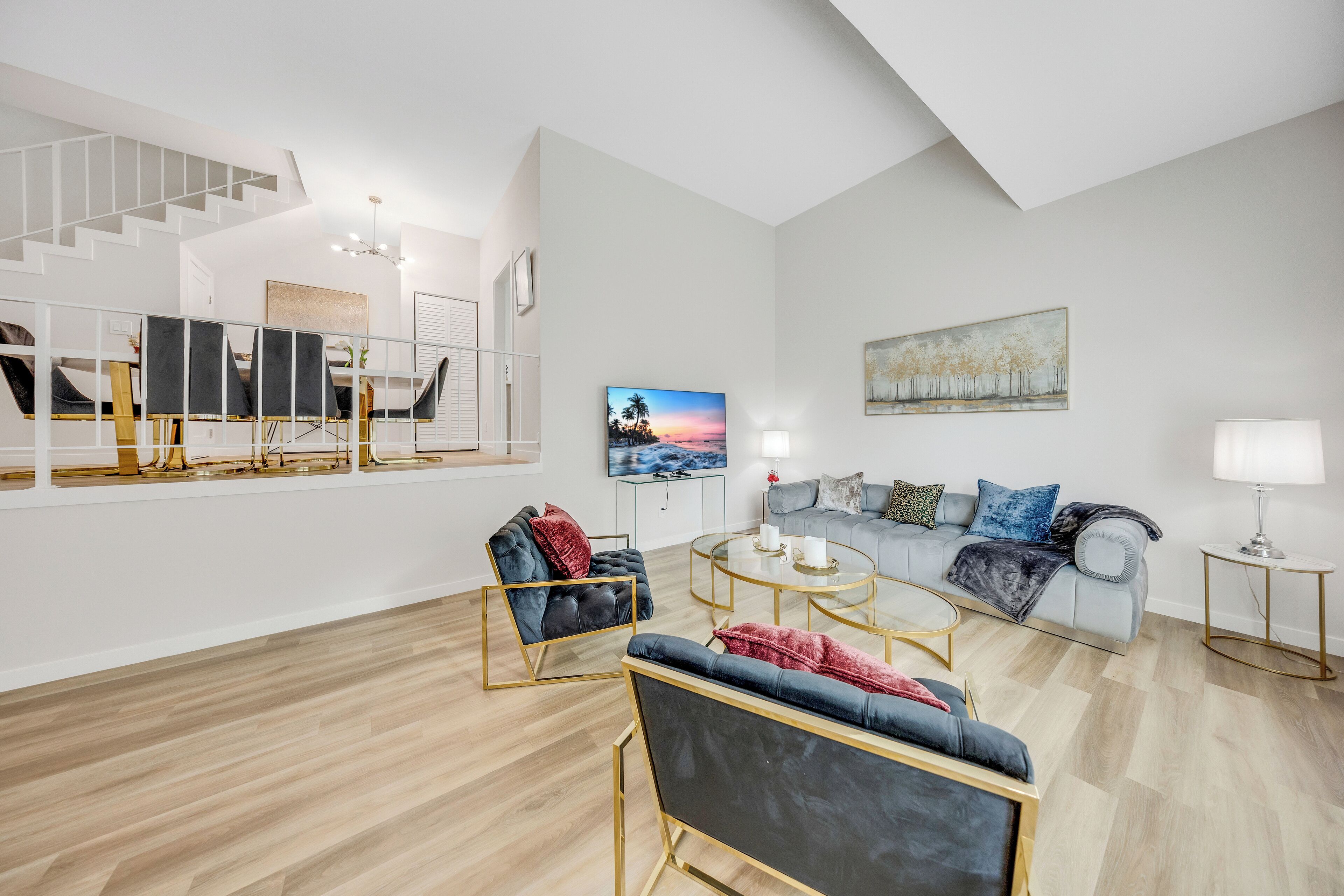 Una sala de estar moderna con una escalera, un conjunto de sofás, una mesa de centro y un cuadro en la pared.