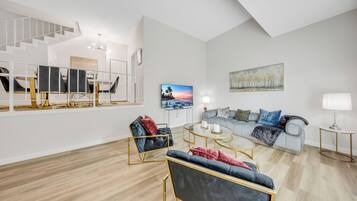 Una sala de estar moderna con una escalera, un conjunto de sofás, una mesa de centro y un cuadro en la pared.