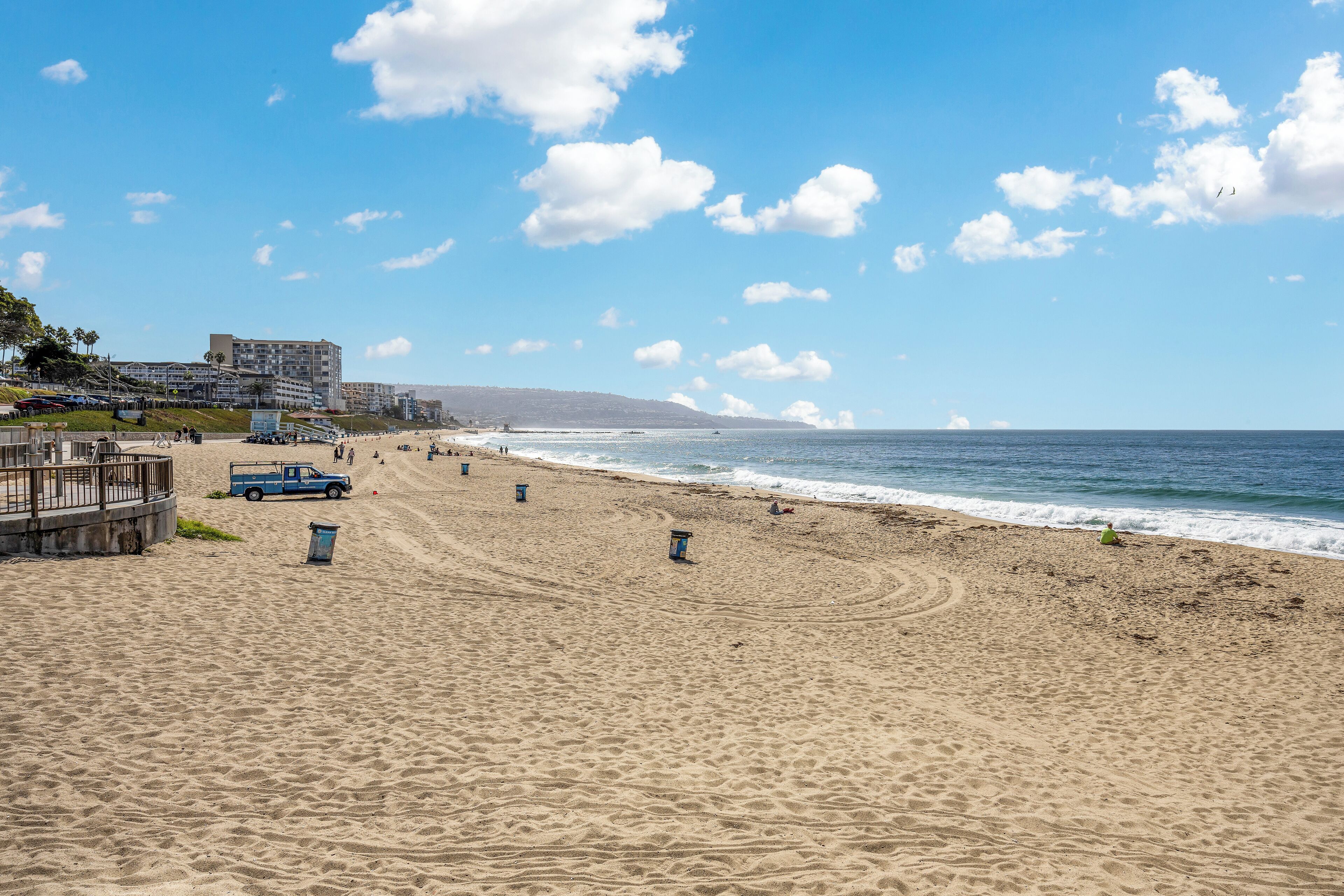 A beach with a wooden walkway, a blue truck, and a building in the background.