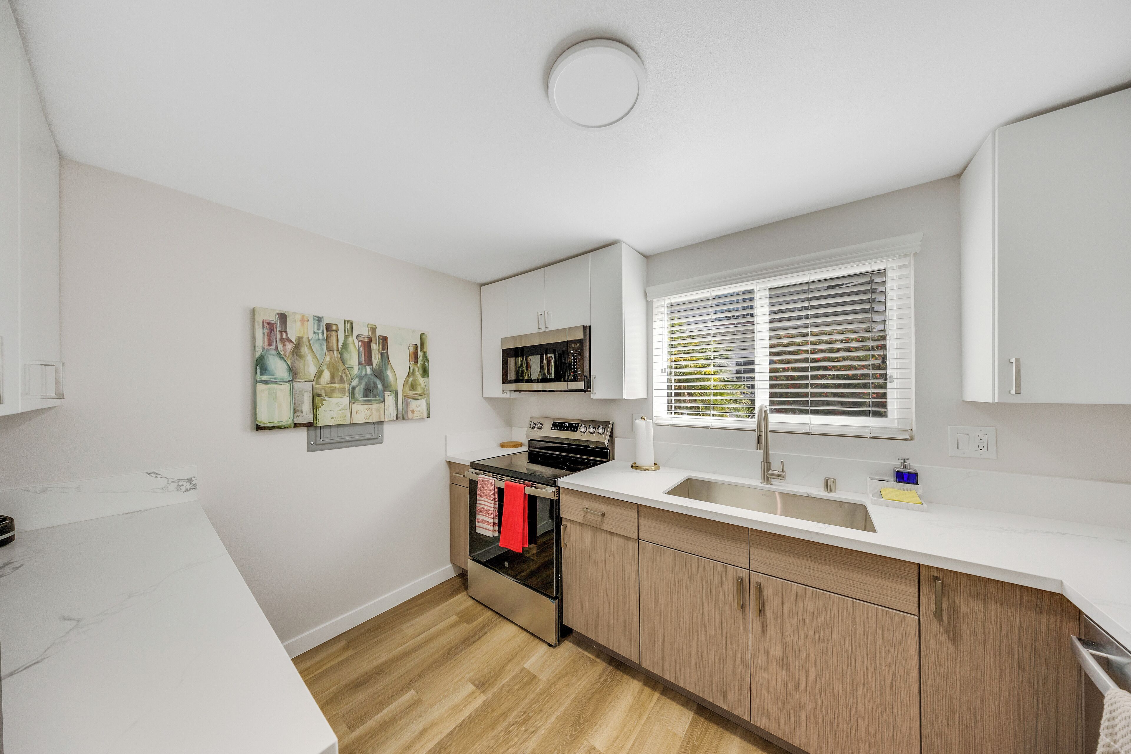 A modern kitchen with white cabinetry, a stainless steel oven, and a window with blinds.