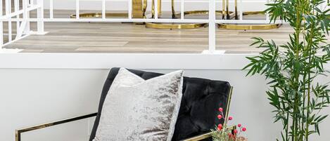 Una sala de estar moderna con un sofá negro, una mesa de centro redonda con marco dorado y un jarrón verde con flores rojas.