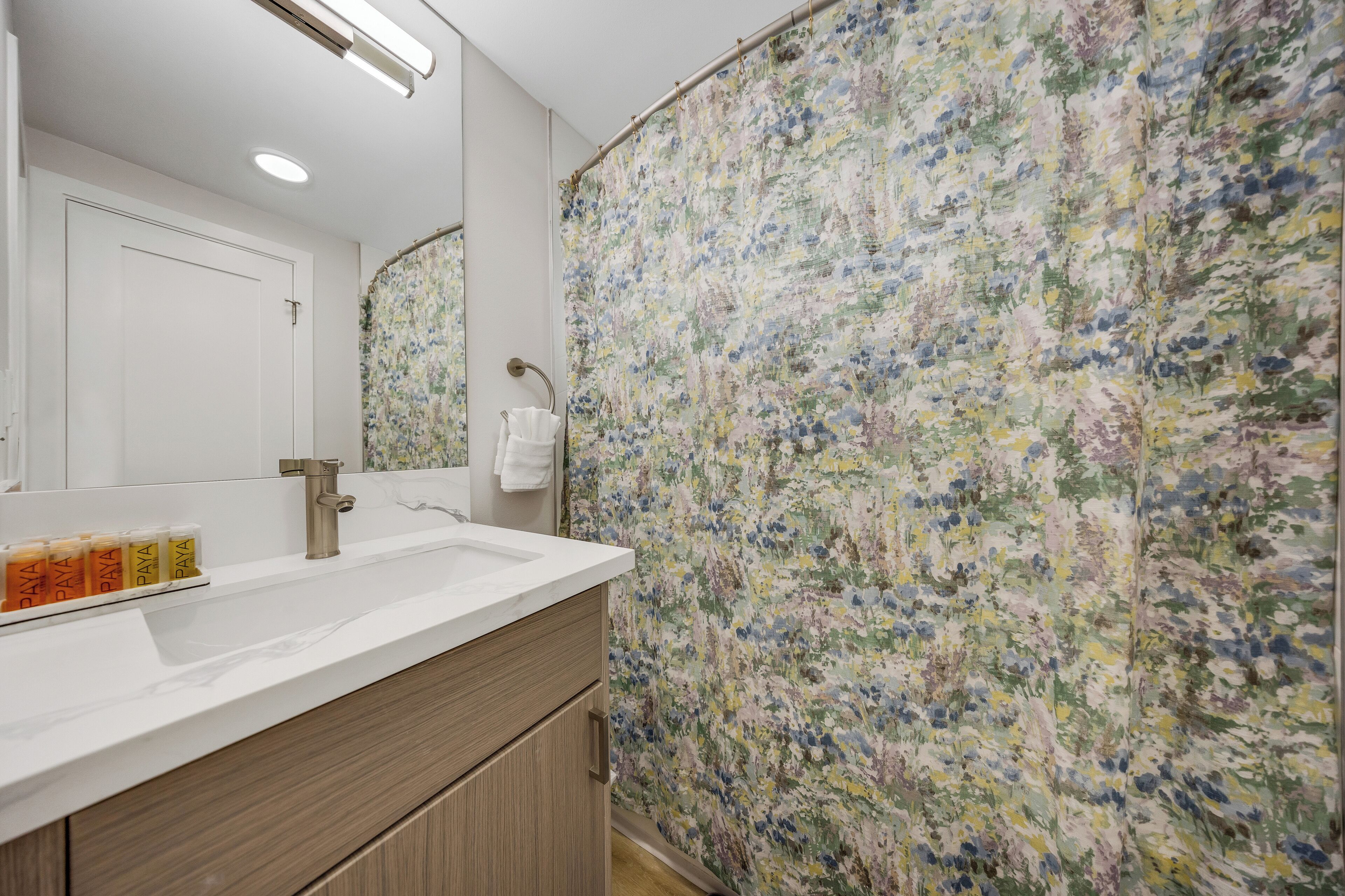 Un baño con lavamanos blanco, espejo y cortina de ducha con estampado floral.