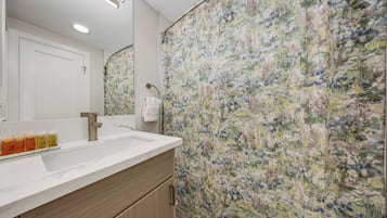 Un baño con lavamanos blanco, espejo y cortina de ducha con estampado floral.