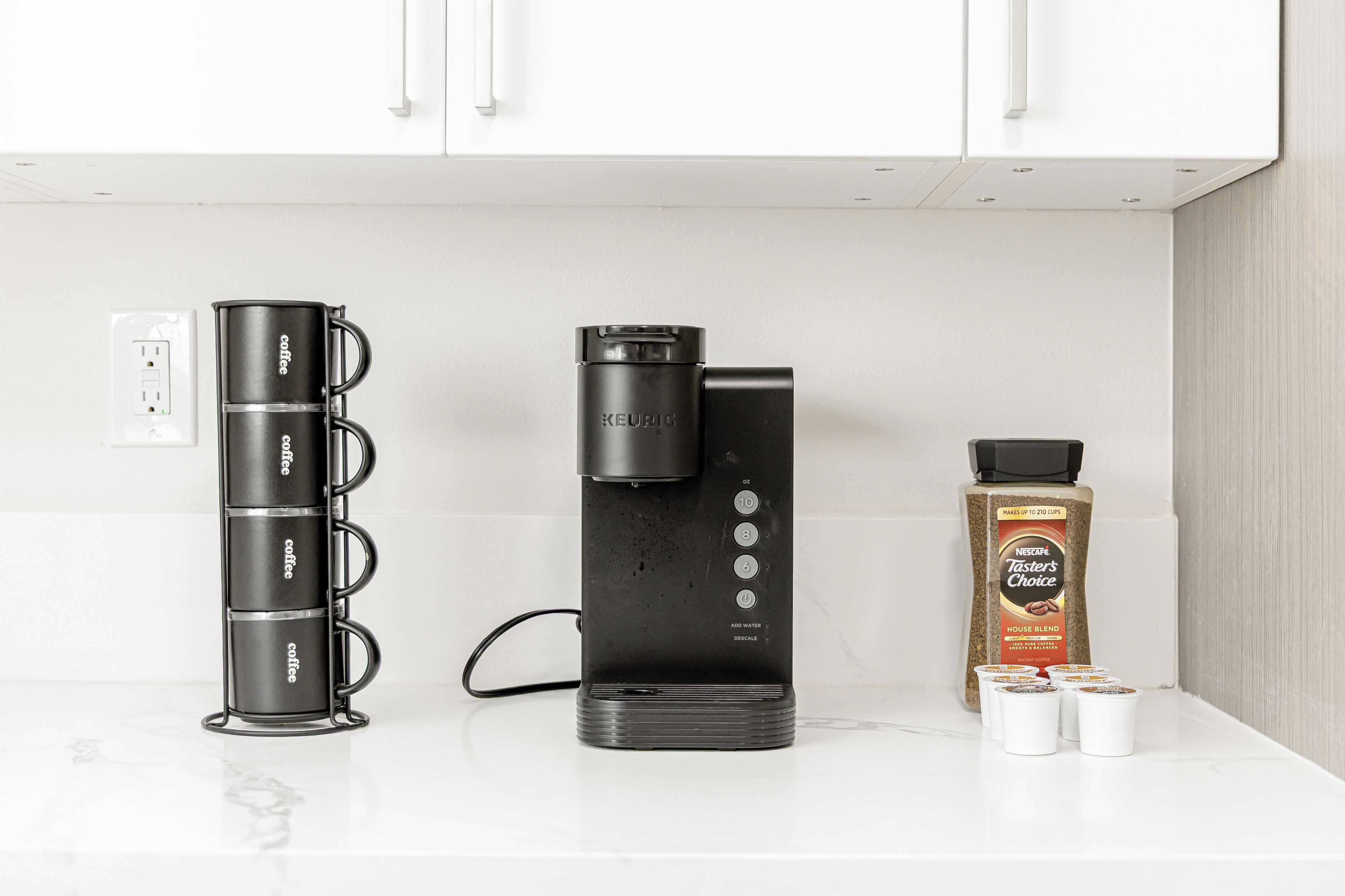 Una cafetera, un dispensador de cápsulas de café y una caja de cápsulas de café sobre una encimera de cocina.