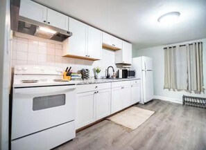 A modern kitchen with white cabinets, a stove, and a microwave. - The Onion Ranch, 2 BED with free onsite parking (Winooski)
