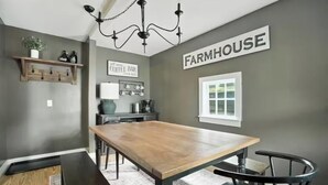 A dining area with a wooden table and chairs, a chandelier, a coffee bar sign, and a 'Farmhouse' sign on the wall.