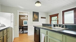 A kitchen with a wooden floor, a sink, and a dishwasher. There is a window with a wooden frame and a door with a frosted glass panel.