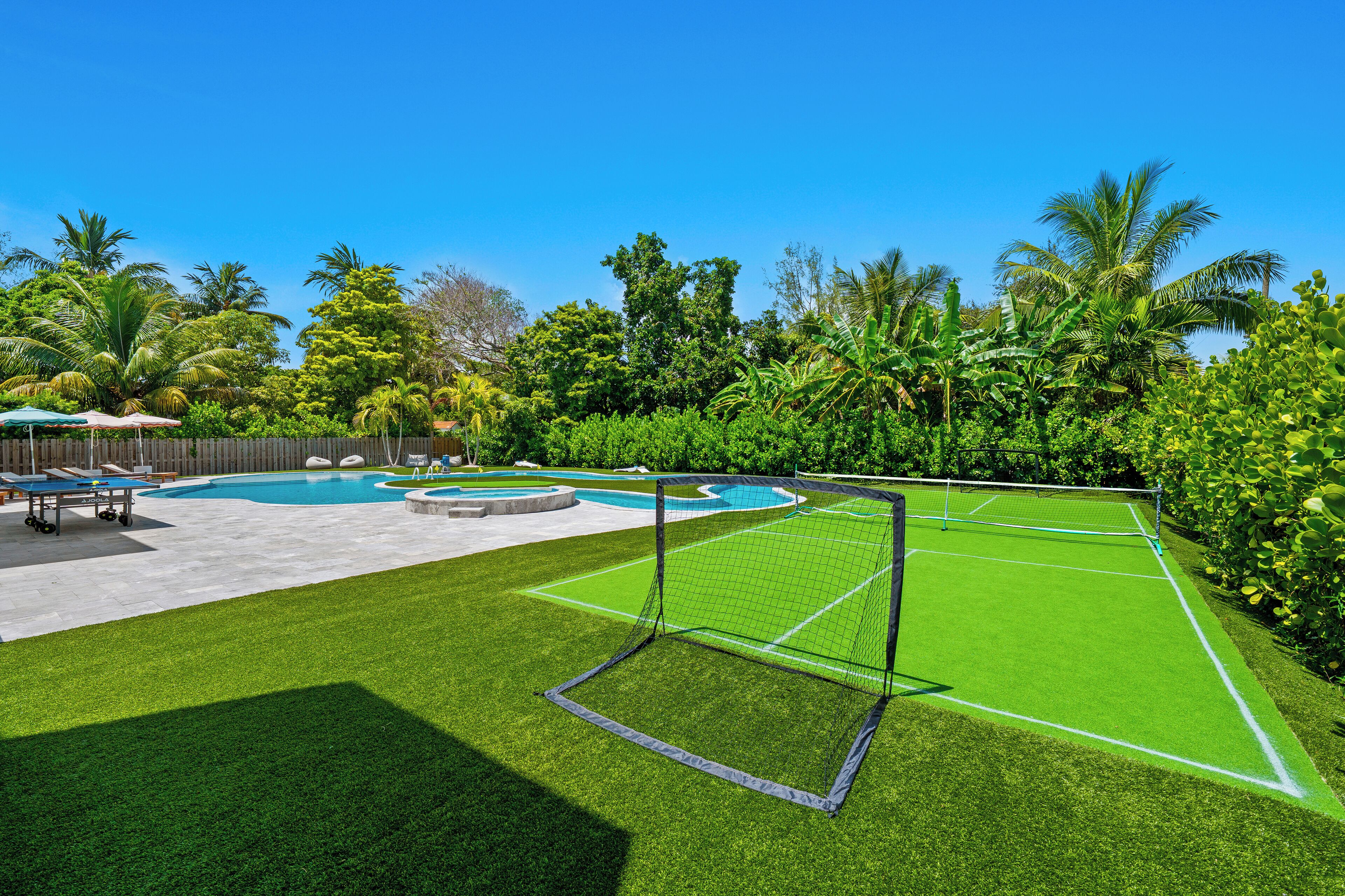 Un giardino sul retro con campo da tennis, piscina e vegetazione rigogliosa.