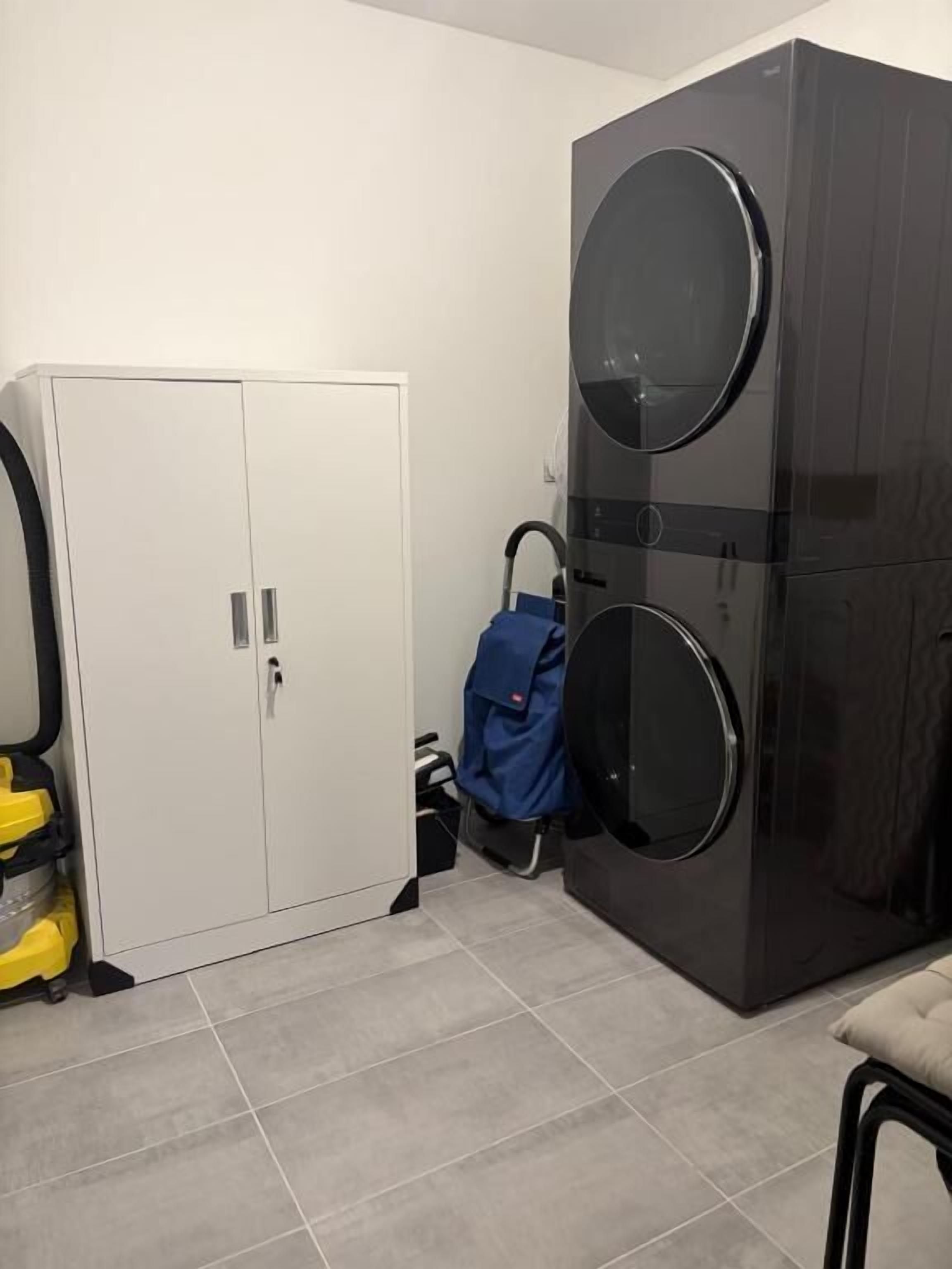 A laundry room with a white cabinet, a large black washing machine, and a blue umbrella.